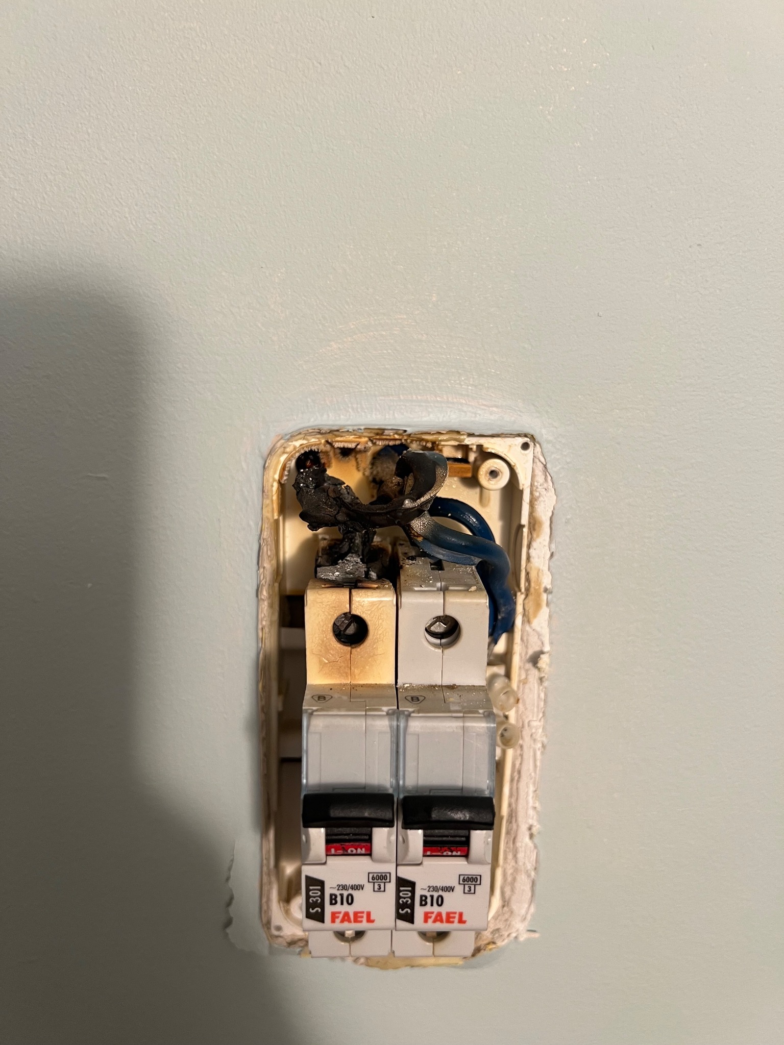 Spalona instalacja elektryczna w ścianie, widoczne stopione elementy i uszkodzone kable. Awaria instalacji, prawdopodobnie zwarcie.