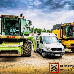 Klimatyzacja Wschód Mobilny Serwis Klimatyzacji - Dwa kombajny (zielony Claas Mega i żółty) oraz biały bus Mercedes Sprinter z otwartymi drzwiami na placu. Logo firmy w prawym dolnym rogu.