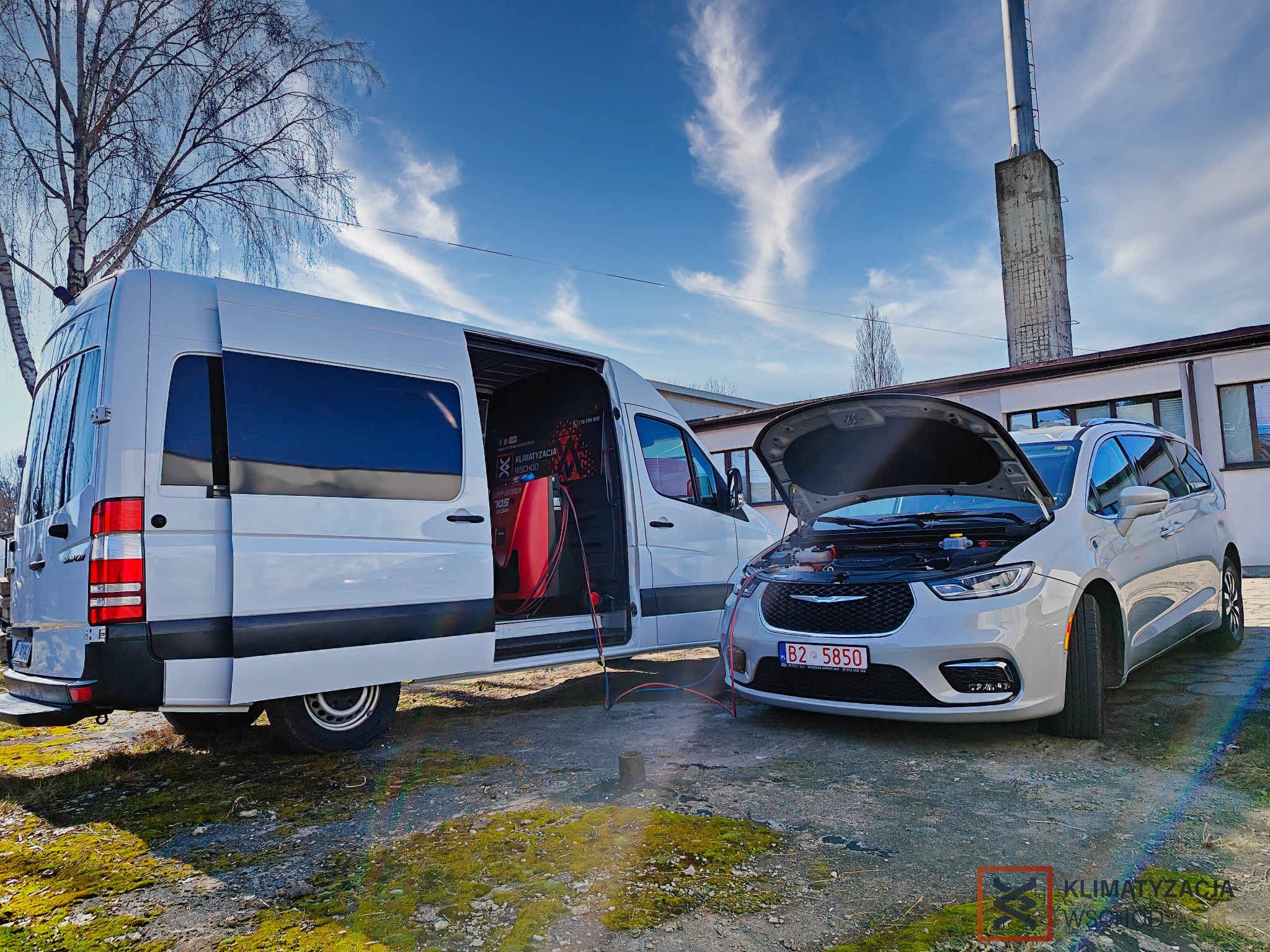 Mobilny serwis klimatyzacji w Białymstoku. Biały van z otwartymi drzwiami i podłączony do srebrnego auta z otwartą maską. Sprzęt serwisowy widoczny wewnątrz vana.