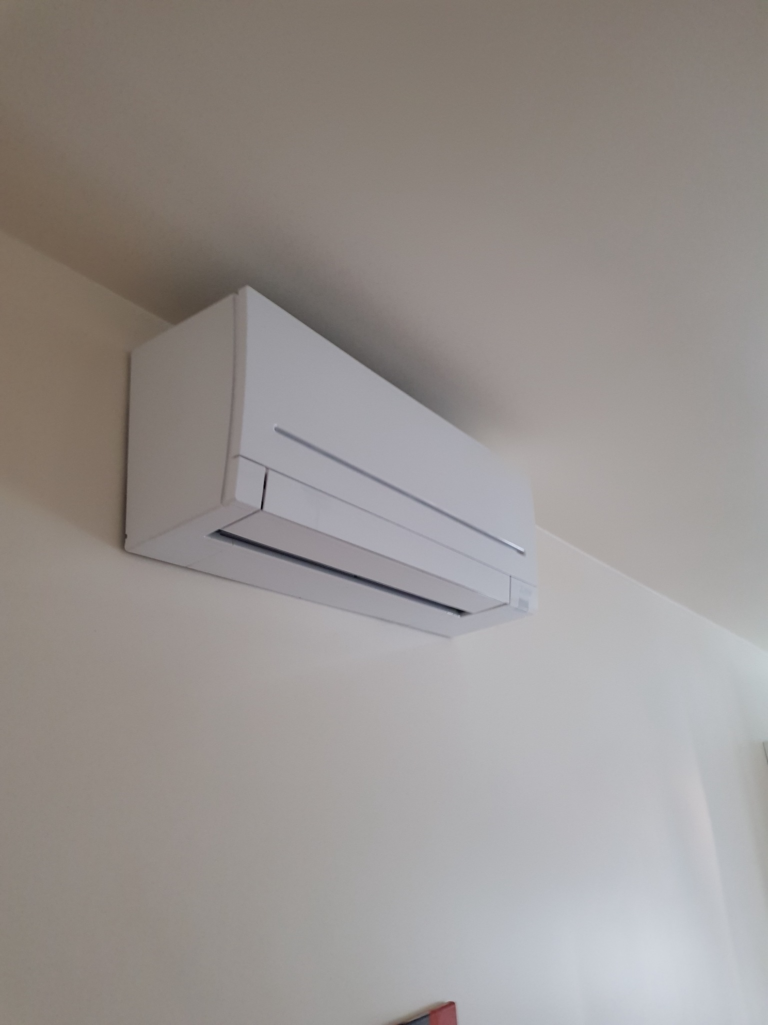 Biały klimatyzator Mitsubishi zamontowany na jasnej ścianie w pomieszczeniu, widok z dołu.