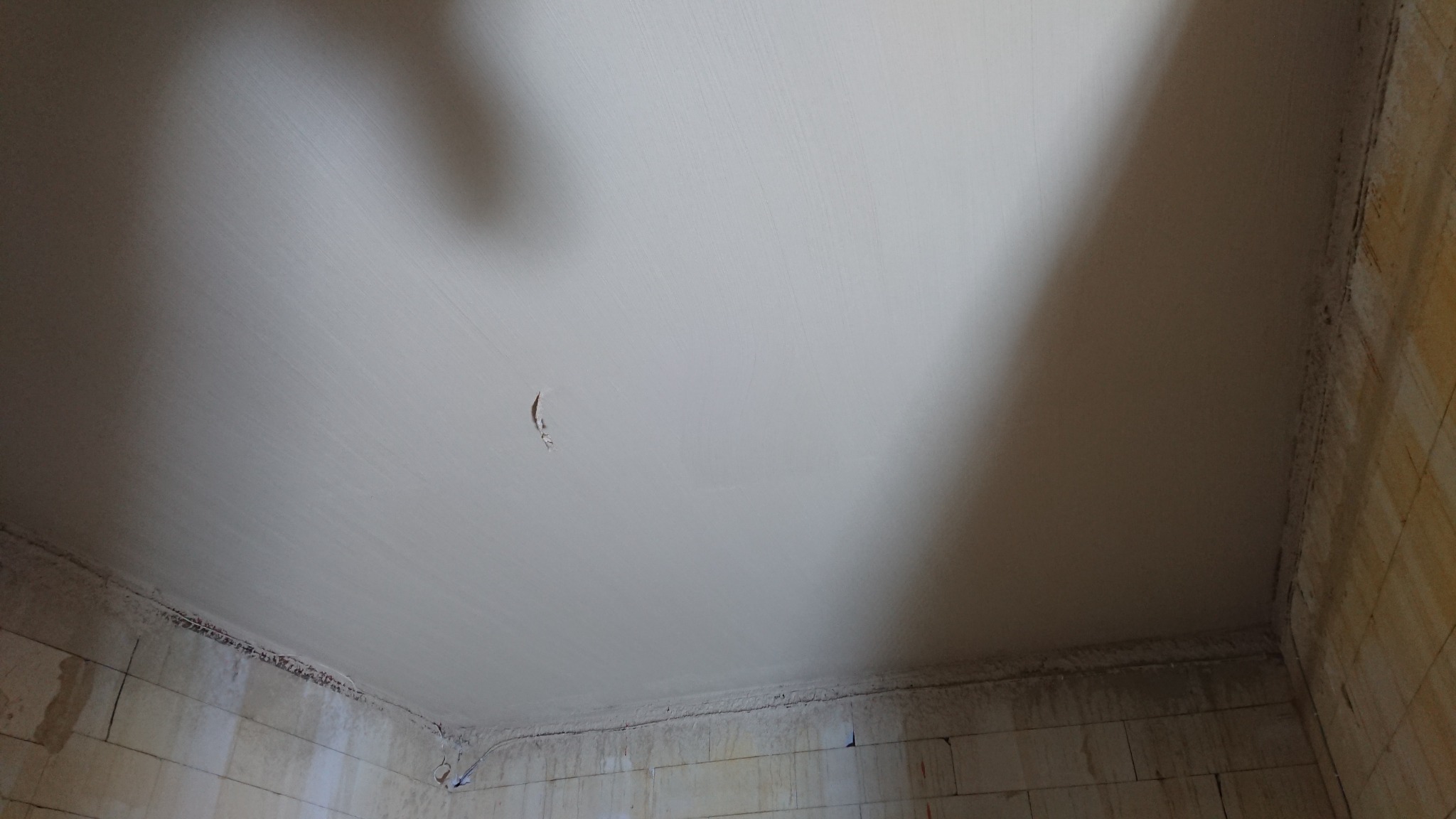 Świeżo nałożona, jasna masa na ścianach i suficie w surowym wnętrzu, widoczne ślady po przewodach elektrycznych i niewielkie niedoskonałości powierzchni.