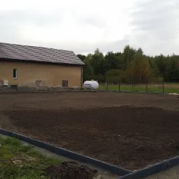 Przygotowany teren pod trawnik z obrzeżami, widoczny budynek mieszkalny i zbiornik na gaz w tle.