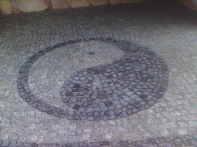 Kostka brukowa ułożona w symbol Yin Yang. Szara kostka tworzy wzór na chodniku. Widok z góry, lekko rozmyty obraz.