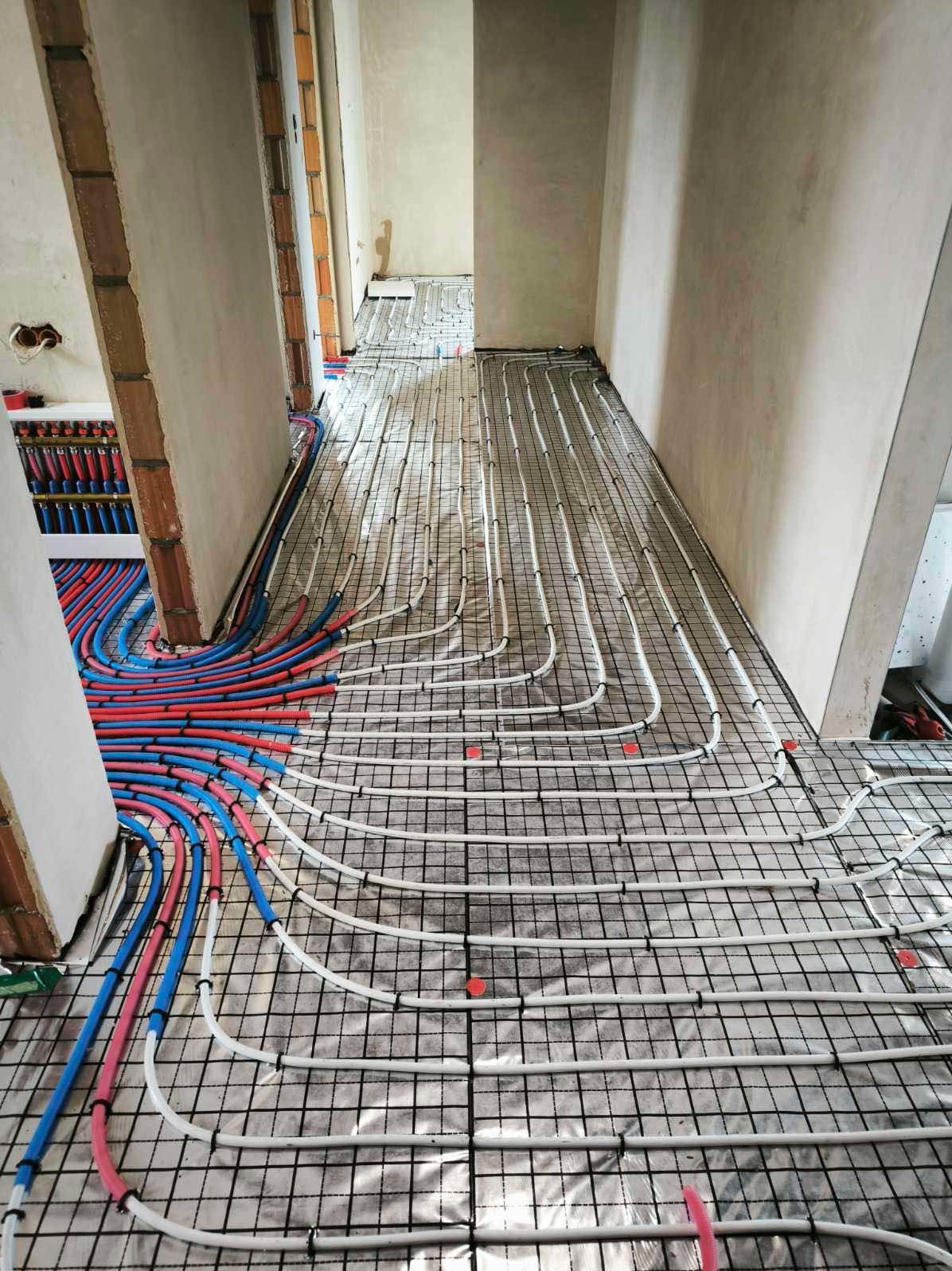 Rozłożona instalacja ogrzewania podłogowego na folii izolacyjnej, rury białe i kolorowe, widok z góry, przygotowanie do wylewki, wnętrze w stanie surowym.