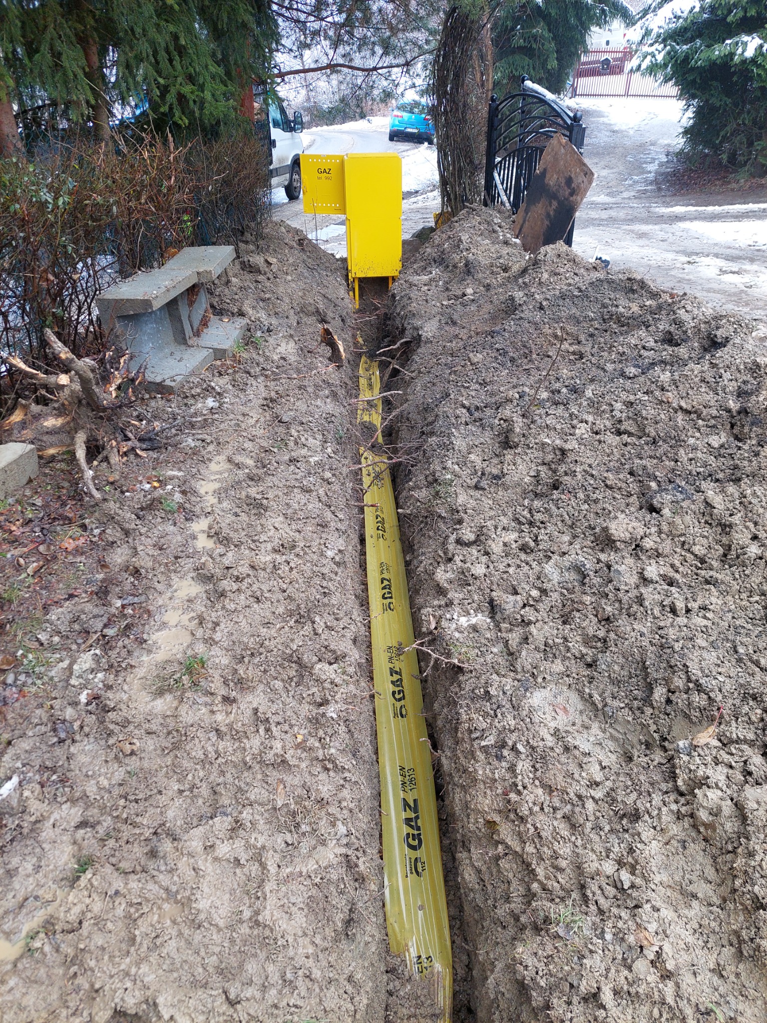 Żółty rurociąg gazowy w wykopie ziemnym, widoczny fragment szafki gazowej, teren po robotach ziemnych.