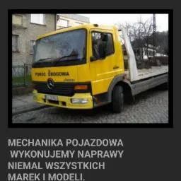 Żółty pojazd pomocy drogowej Mercedes-Benz z napisem 'Pomoc Drogowa' i numerem telefonu, zaparkowany na ulicy w mieście.
