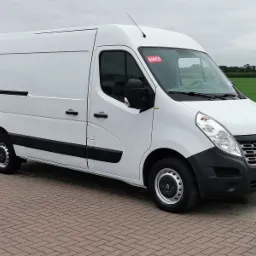 Biały Renault Master z wysokim dachem, zaparkowany na brukowanej powierzchni z zielonym polem w tle, widoczna naklejka 'AIRCO' na szybie.