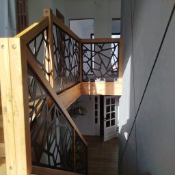 Siepak - Stalowe Realizacje - Drewniane schody z nowoczesną, czarną balustradą o ażurowym wzorze, prowadzące na dół. Widok z góry, jasne oświetlenie, minimalistyczny design.