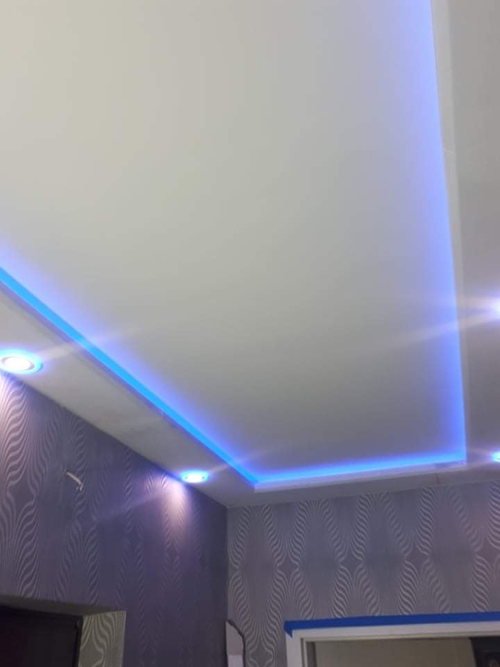 Sufit podwieszany z oświetleniem LED w kolorze niebieskim, dekoracyjne tapety na ścianach z wzorem falistym w odcieniach szarości i srebra.