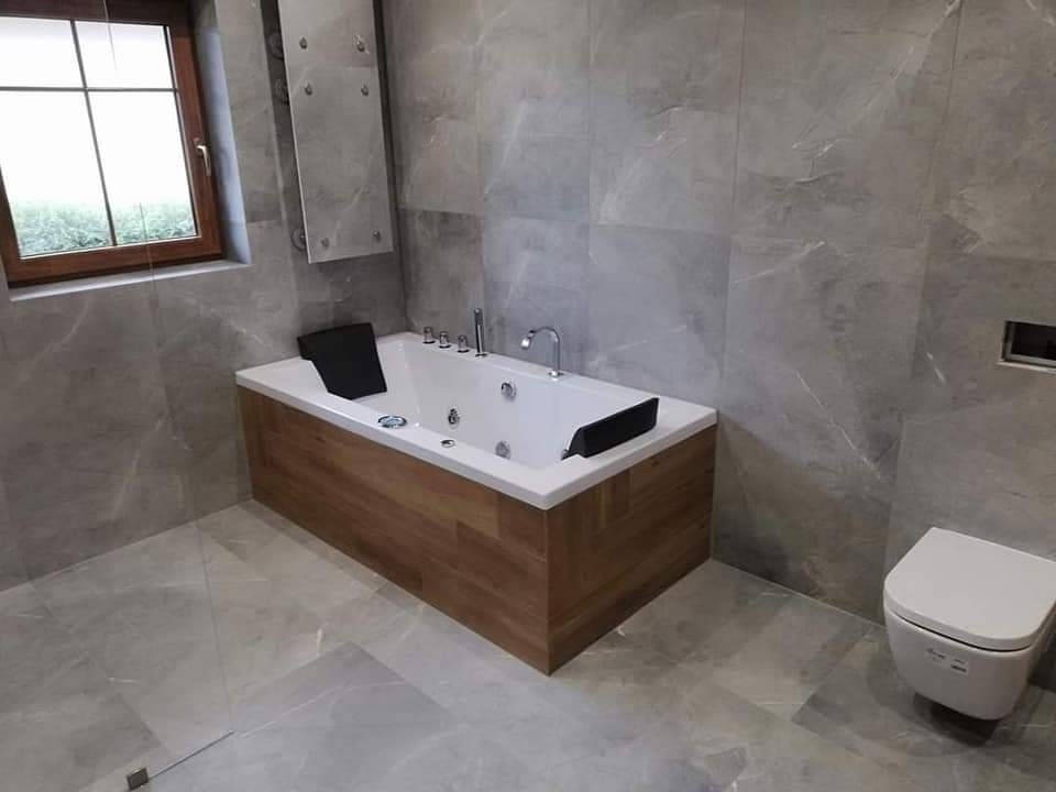 Nowoczesna łazienka z marmurowymi płytkami, drewnianą obudową wanny z hydromasażem i podwieszaną toaletą.