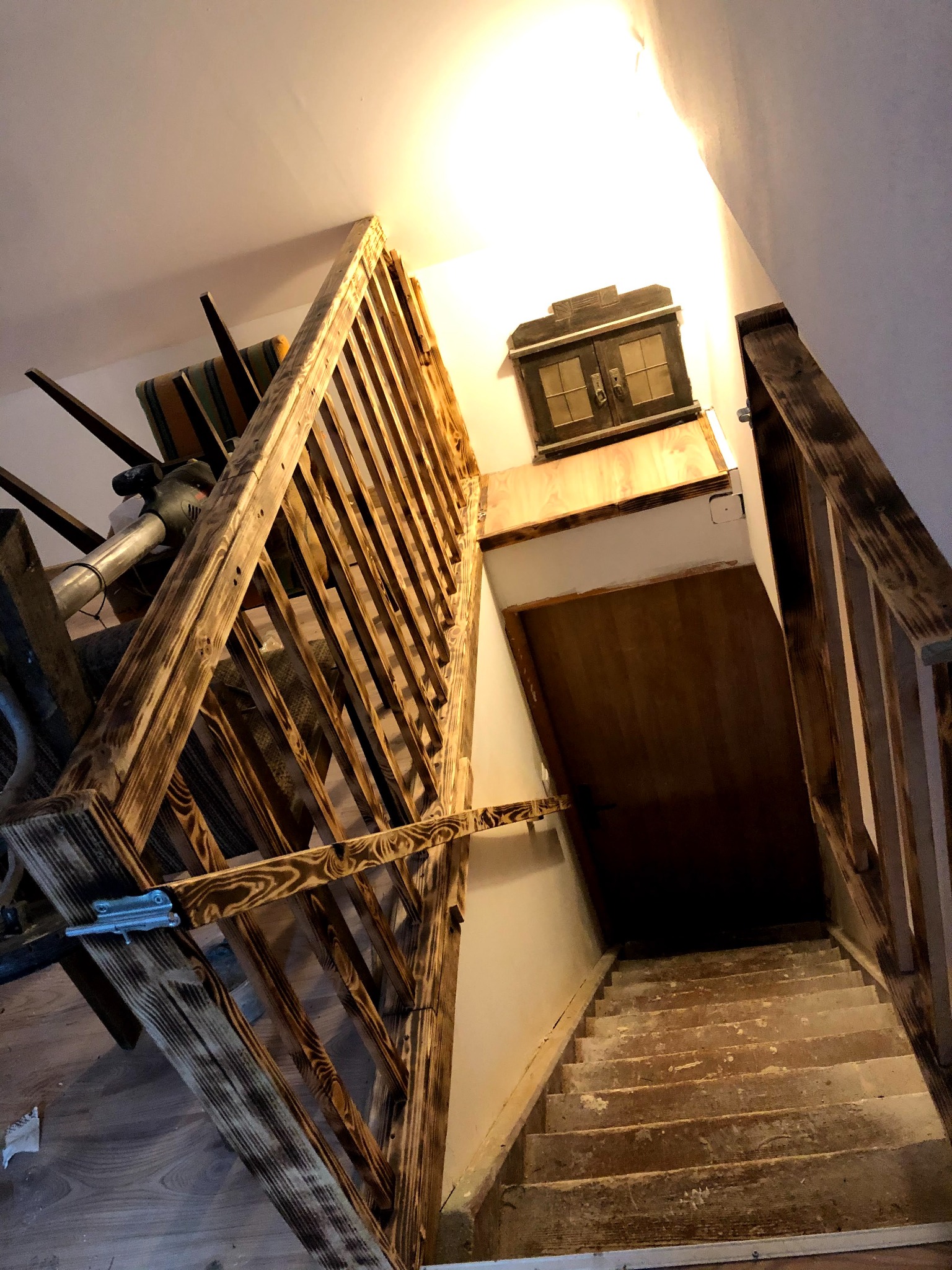 Drewniane schody z balustradą w trakcie prac wykończeniowych, widoczne ślady po szpachlowaniu na stopniach, obok schodów odkurzacz i krzesło.