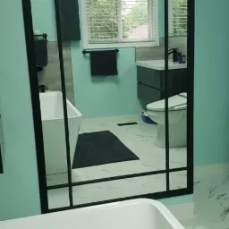 Nowoczesna łazienka z turkusowymi ścianami, białą wanną, szafką z umywalką i czarnymi akcentami, widoczna w lustrze z czarną ramą