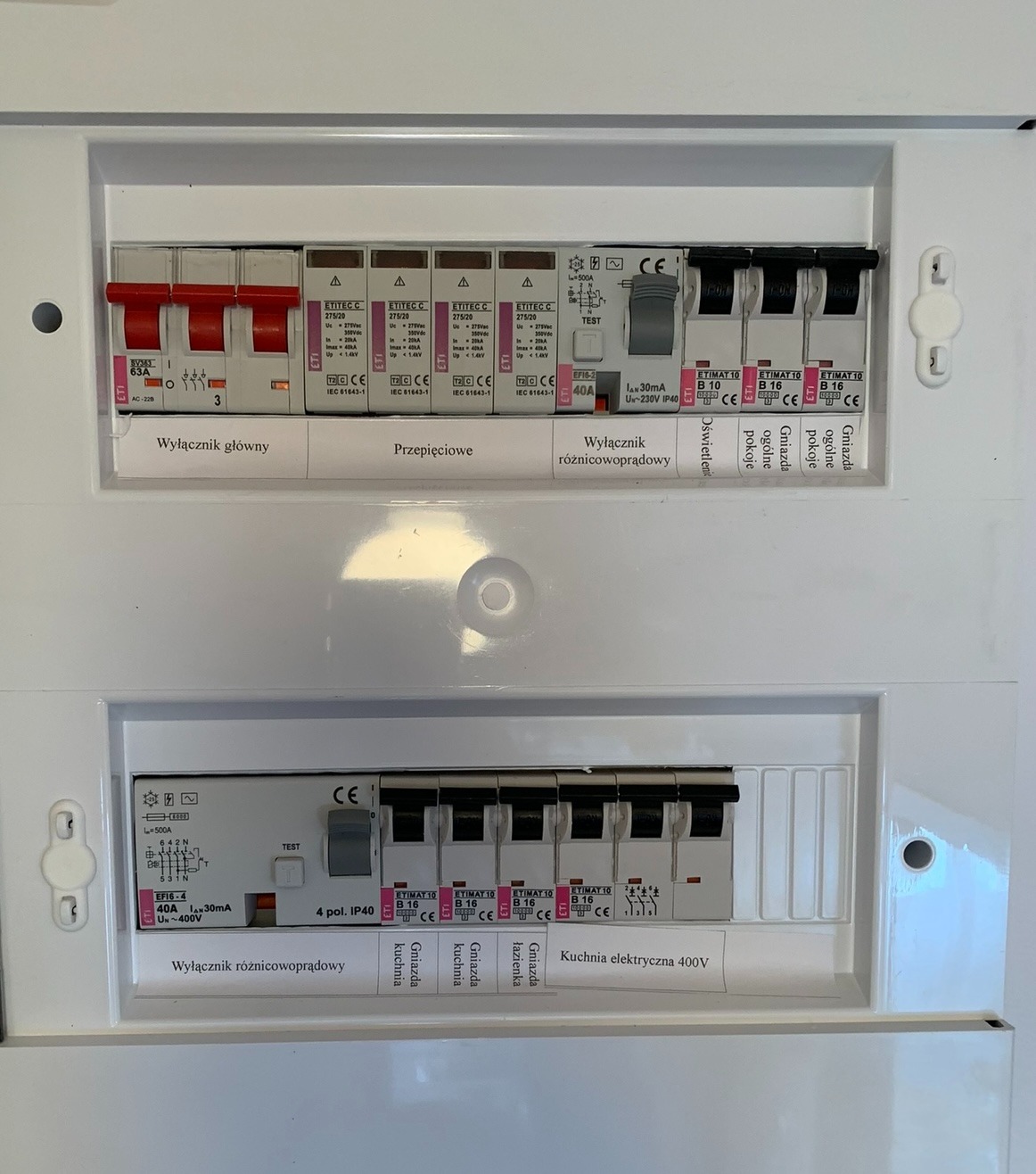 Rozdzielnica elektryczna z bezpiecznikami i wyłącznikami różnicowoprądowymi, opisane obwody: oświetlenie, gniazda pokojowe, kuchnia 400V, zabezpieczenia przepięciowe.