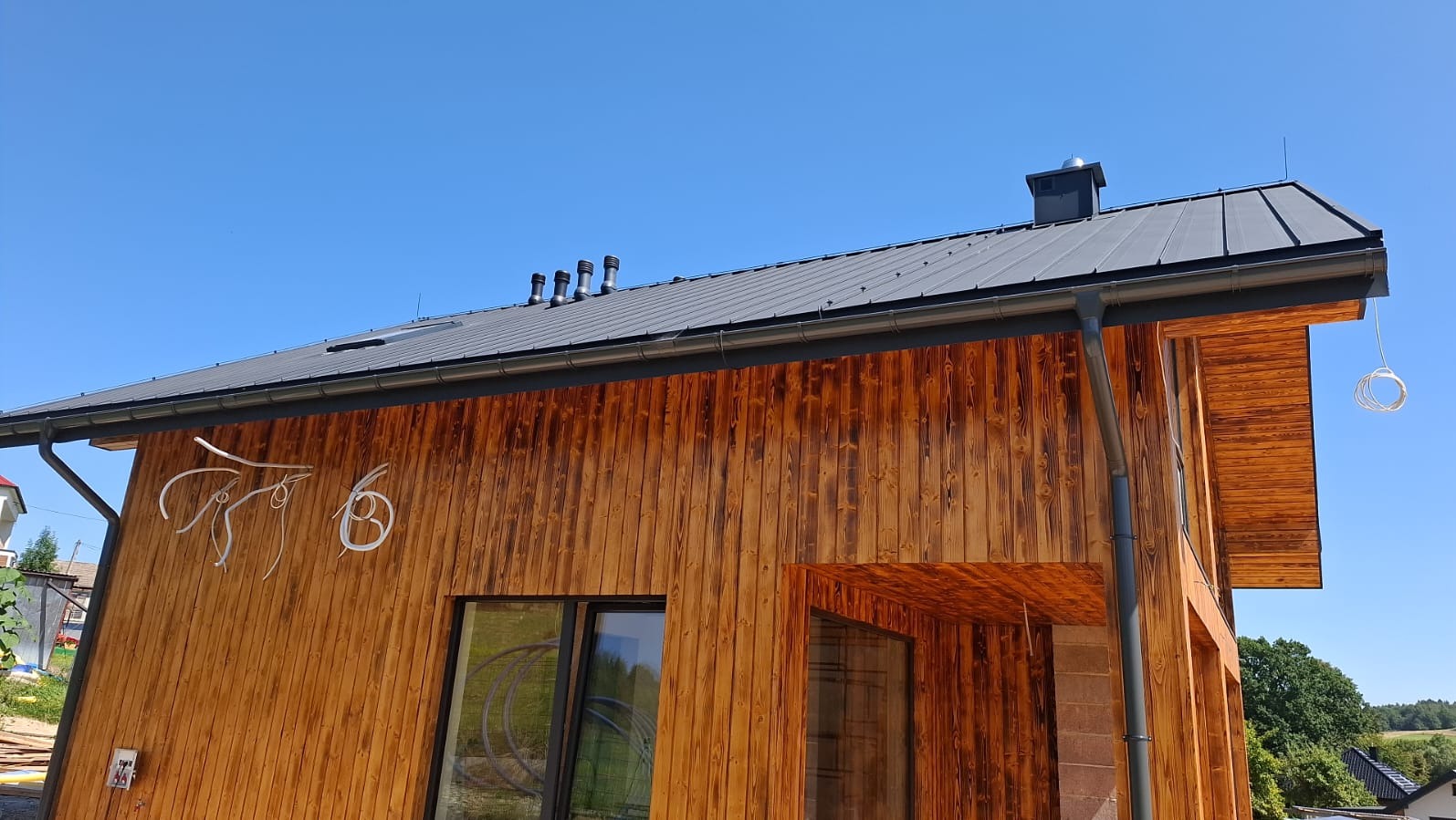 Nowoczesny dom z drewnianą elewacją i instalacją odgromową na dachu, widoczny z niskiej perspektywy, na tle błękitnego nieba.