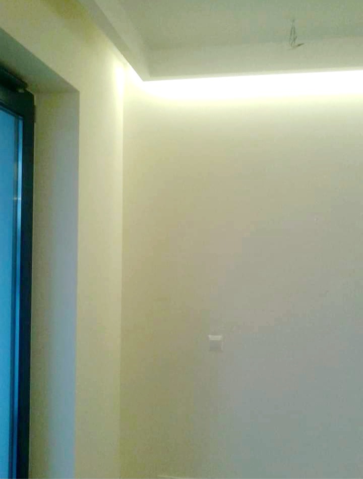 Świeżo pomalowane wnętrze z ukrytym oświetleniem LED w suficie, widoczny fragment drzwi z ciemną ramą i gładka, jasna ściana.