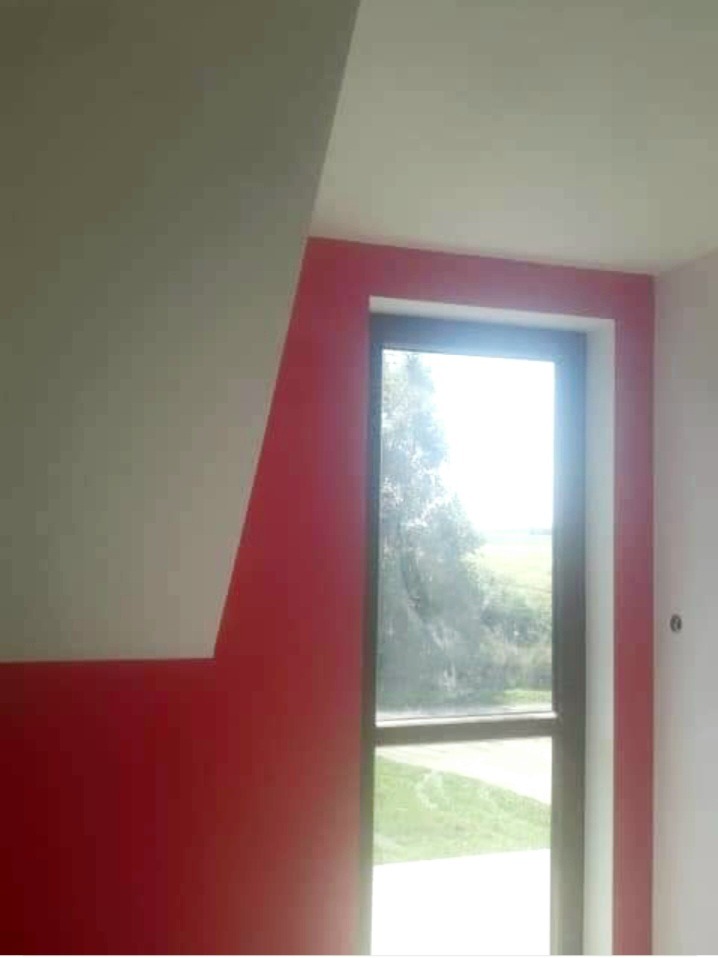 Pomalowane na czerwono ściany w pokoju na poddaszu z oknem, widok na zielony krajobraz za oknem.