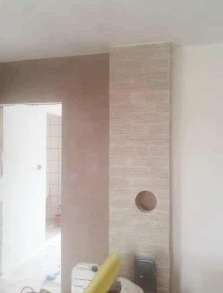 Wnętrze w trakcie prac wykończeniowych: ściana z nałożoną gładzią szpachlową w odcieniach beżu, fragment ściany z otworem, widoczne narzędzia malarskie i wiadro z farbą.