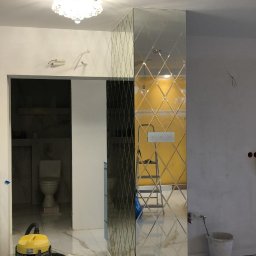 RANEX Sp. z o.o. - Ściana wykończona lustrzanymi płytkami ułożonymi w romby, widoczny odkurzacz, wiadro i drabina w tle, marmurowa podłoga, sufit z żyrandolem
