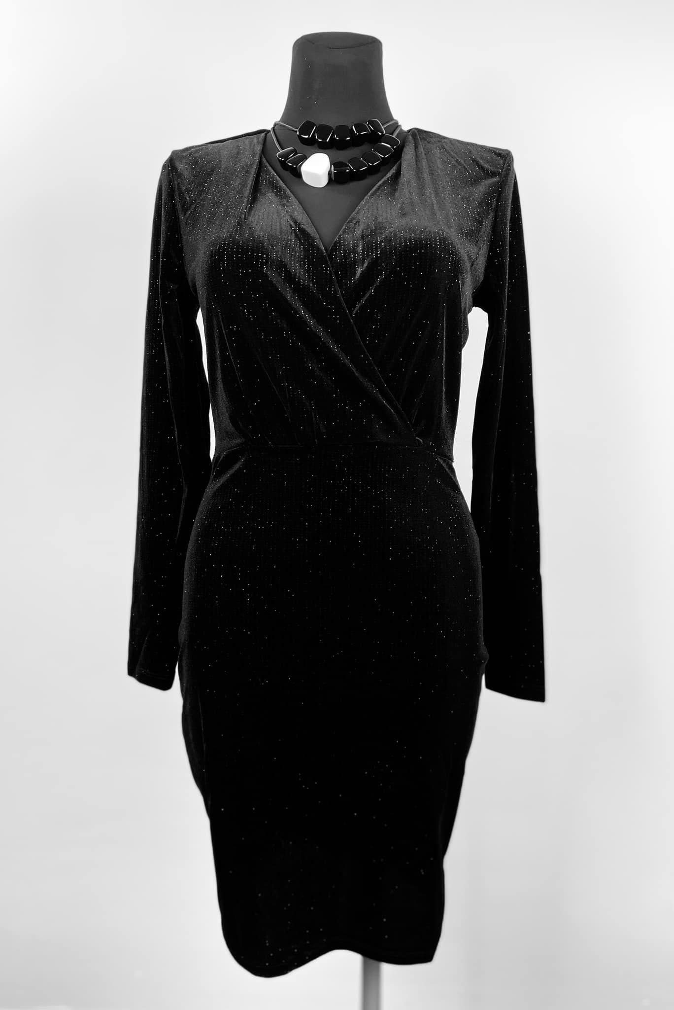 Czarna, welurowa sukienka z długim rękawem i kopertowym dekoltem, prezentowana na manekinie z czarno-białym naszyjnikiem.