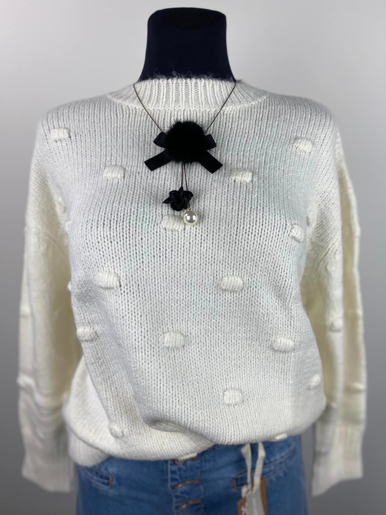 Kremowy sweter z dzianiny z wypukłymi aplikacjami w kropki i czarnym naszyjnikiem z kwiatem i perłą, prezentowany na manekinie.