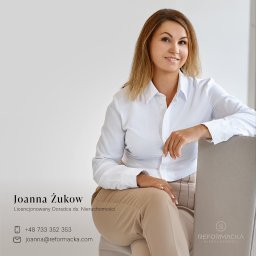 Reformacka Nieruchomości - Portret uśmiechniętej, licencjonowanej doradczyni ds. nieruchomości Joanny Żukow, siedzącej na krześle z logo Reformacka Nieruchomości, w jasnej koszuli i beżowych spodniach.