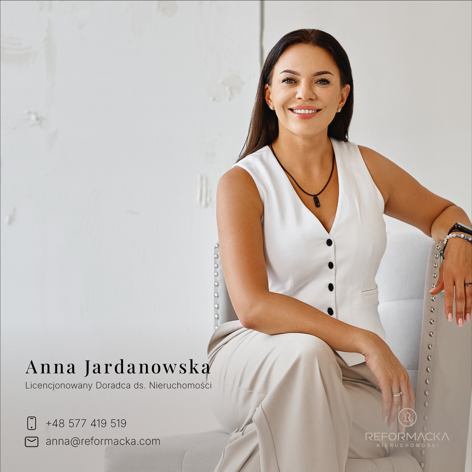 Portret uśmiechniętej, licencjonowanej doradczyni ds. nieruchomości, Anny Jardanowskiej, w białej kamizelce i beżowych spodniach, siedzącej w fotelu z ozdobnymi nitami, na jasnym tle.