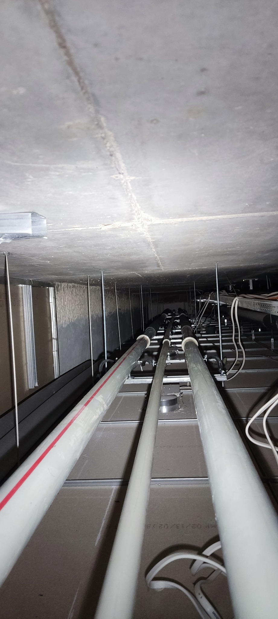 Montaż instalacji podwieszonych pod stropem, widoczne rury z czerwoną linią, metalowe wsporniki i kable elektryczne.