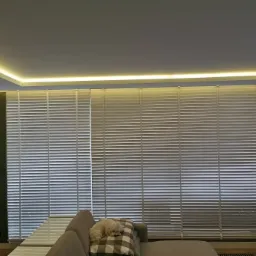 Jasne, drewniane żaluzje poziome w salonie z oświetleniem LED podsufitowym i psem śpiącym na kanapie.