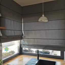 Szare, poziomo fałdowane zasłony w stylu rzymskim zamontowane w oknach nad kuchennym zlewem, widoczne kwiaty w doniczkach na parapecie.