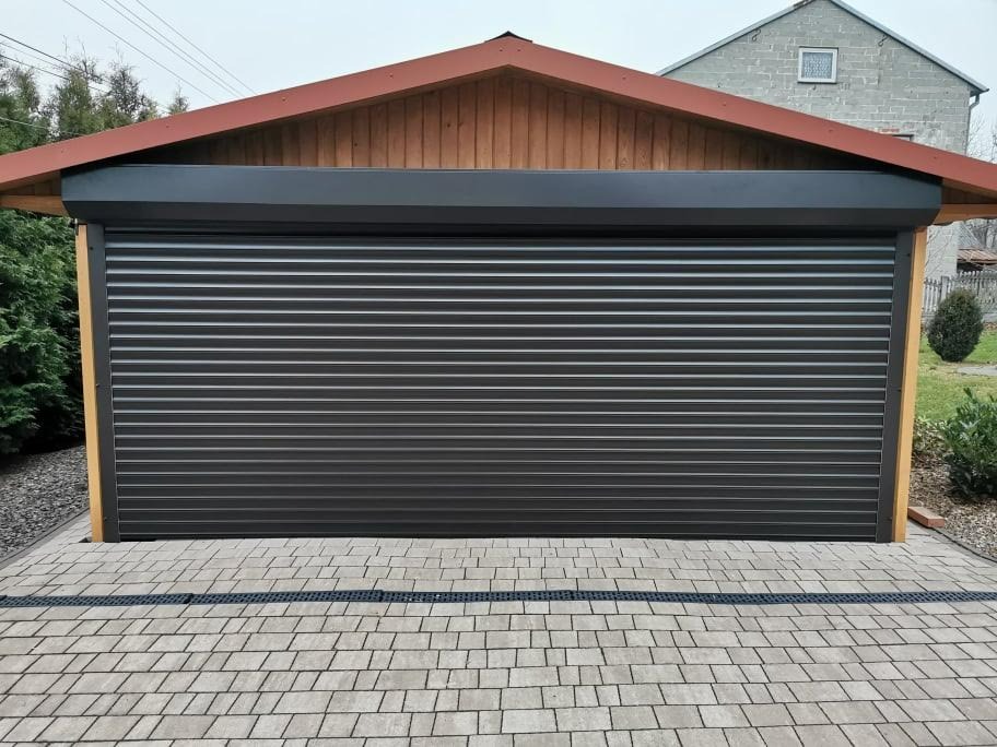 Zasłonięta, ciemna roleta zewnętrzna na drewnianym garażu, widok z poziomu kostki brukowej.