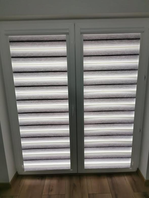 Zamknięte dwuskrzydłowe okno z zamontowanymi roletami dzień noc w odcieniach szarości i bieli, widoczne poziome pasy.