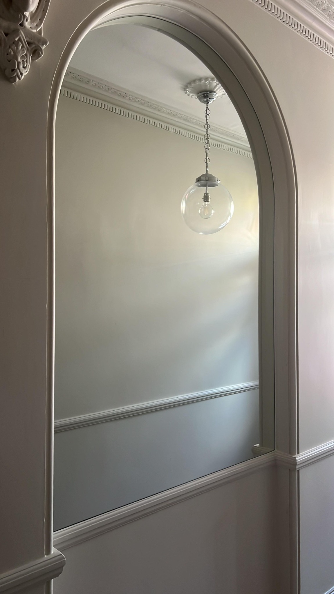 Arched entryway with decorative molding, freshly painted walls, and a modern pendant light with a clear glass globe.