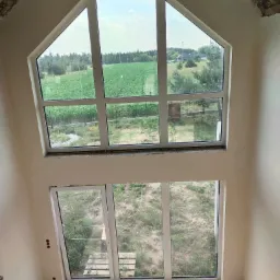 Wysokie okno szczytowe z widokiem na pole, po tynkowaniu maszynowym ścian wewnętrznych, widoczne ślady po pracach wykończeniowych na podłodze.