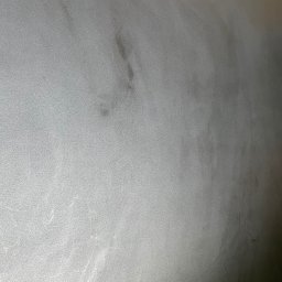 Woodstrug - Szara, gładka powierzchnia z delikatną teksturą i ciemniejszymi smugami, przypominająca wykończenie podłogi lub ściany.