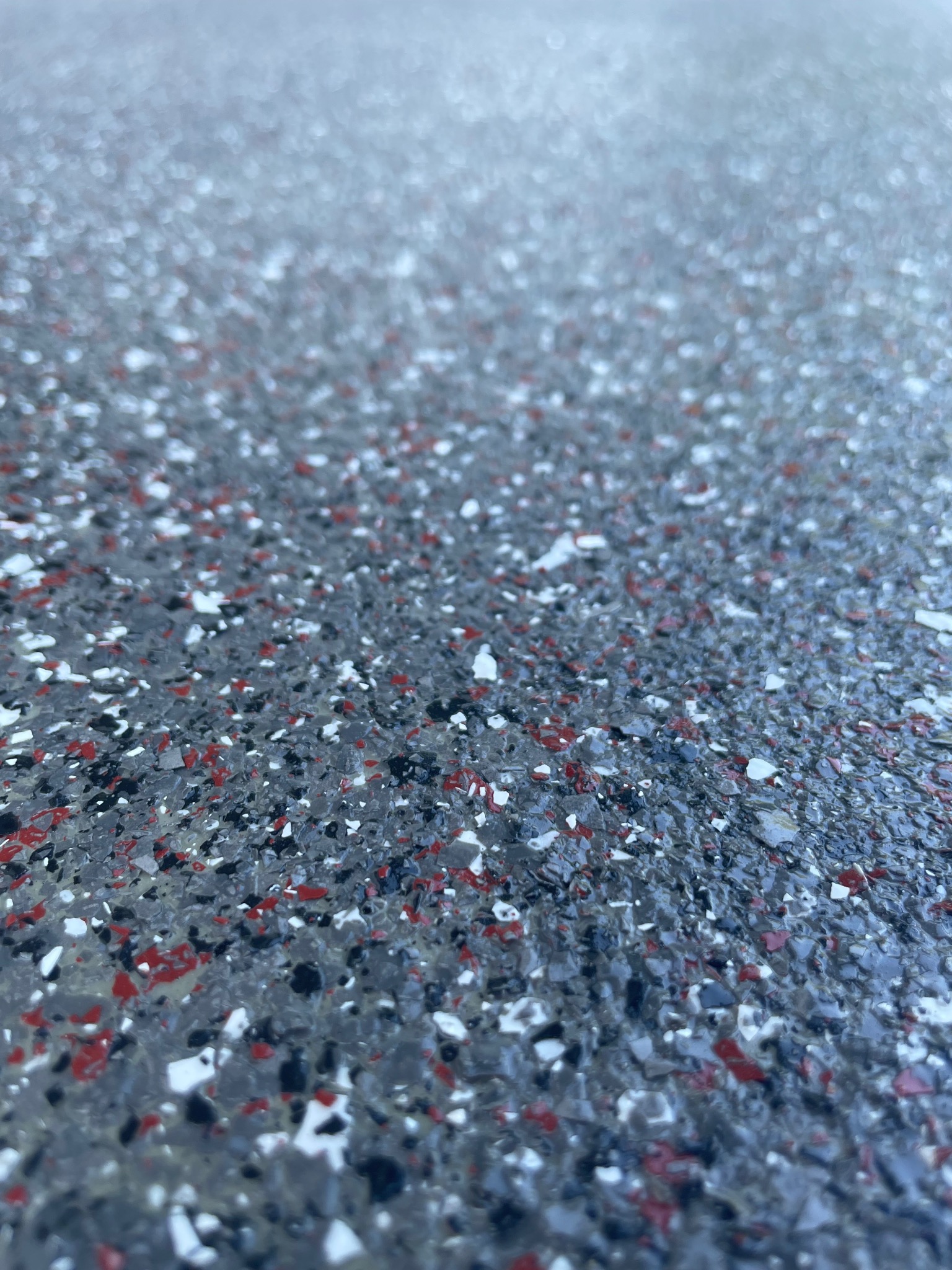 Szara posadzka z zatopionymi płatkami w kolorach czerwonym, białym i czarnym, sfotografowana pod kątem, ukazująca fakturę i głębię.