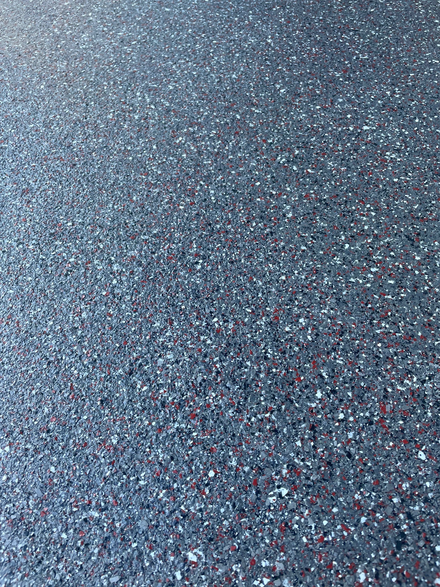 Szara posadzka z widocznymi czerwonymi i białymi drobinami, wykonana w technologii bezspoinowej, prezentowana pod kątem z bliska.