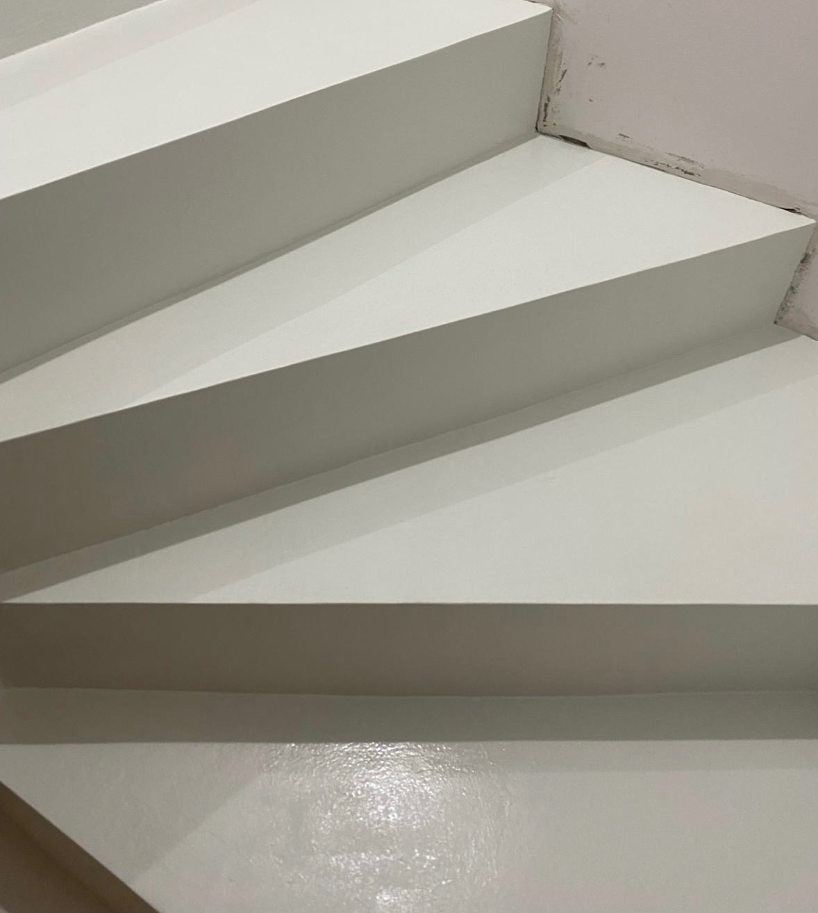 Białe schody pokryte błyszczącą, jednolitą powłoką, widoczne z dołu pod kątem, z niedoskonałościami wykończenia przy ścianie.