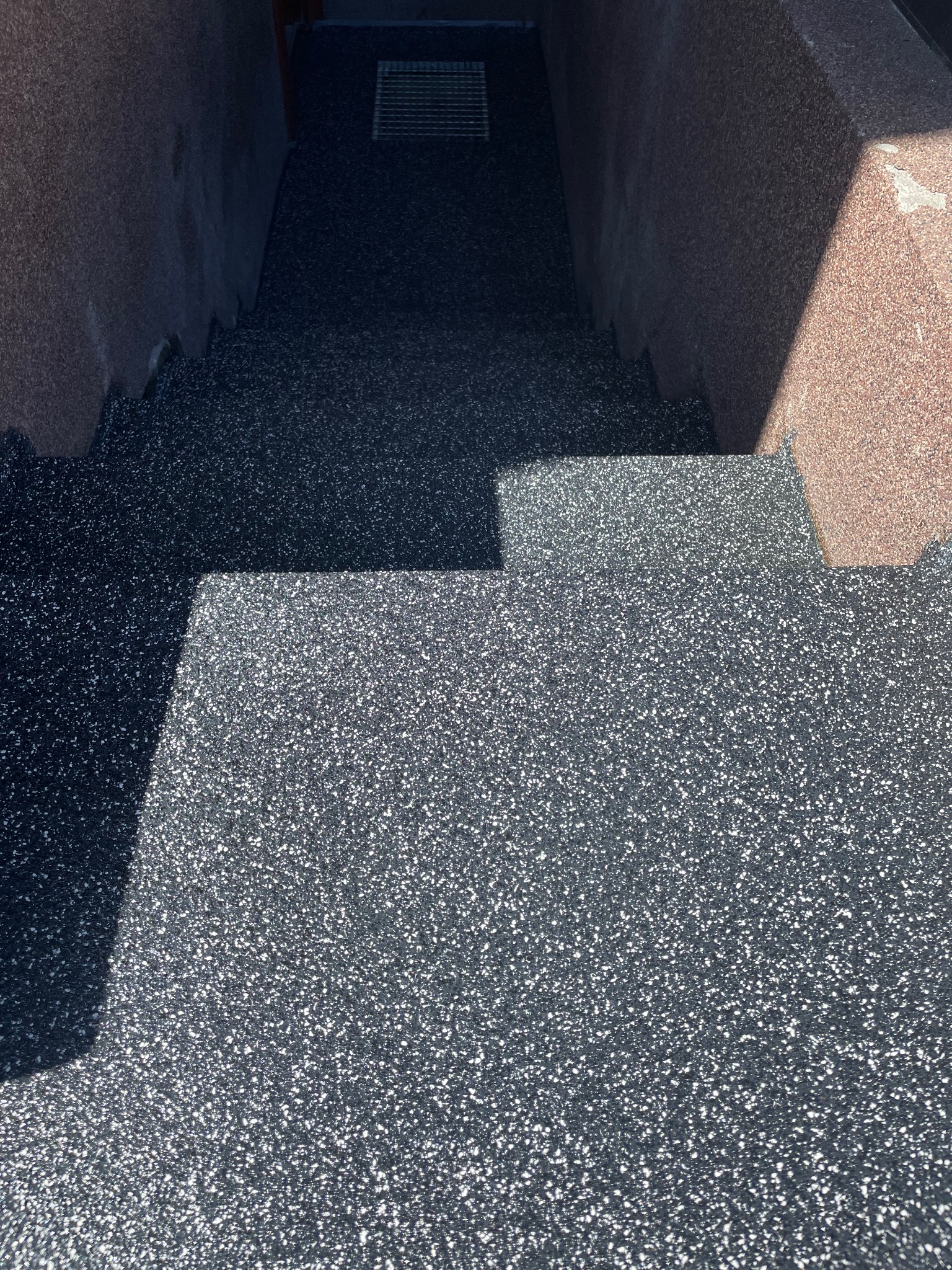 Schody wejściowe z szarą, drobnoziarnistą nawierzchnią w Rumii, prowadzące w dół, z widoczną kratką odpływową i fragmentami ścian po bokach.