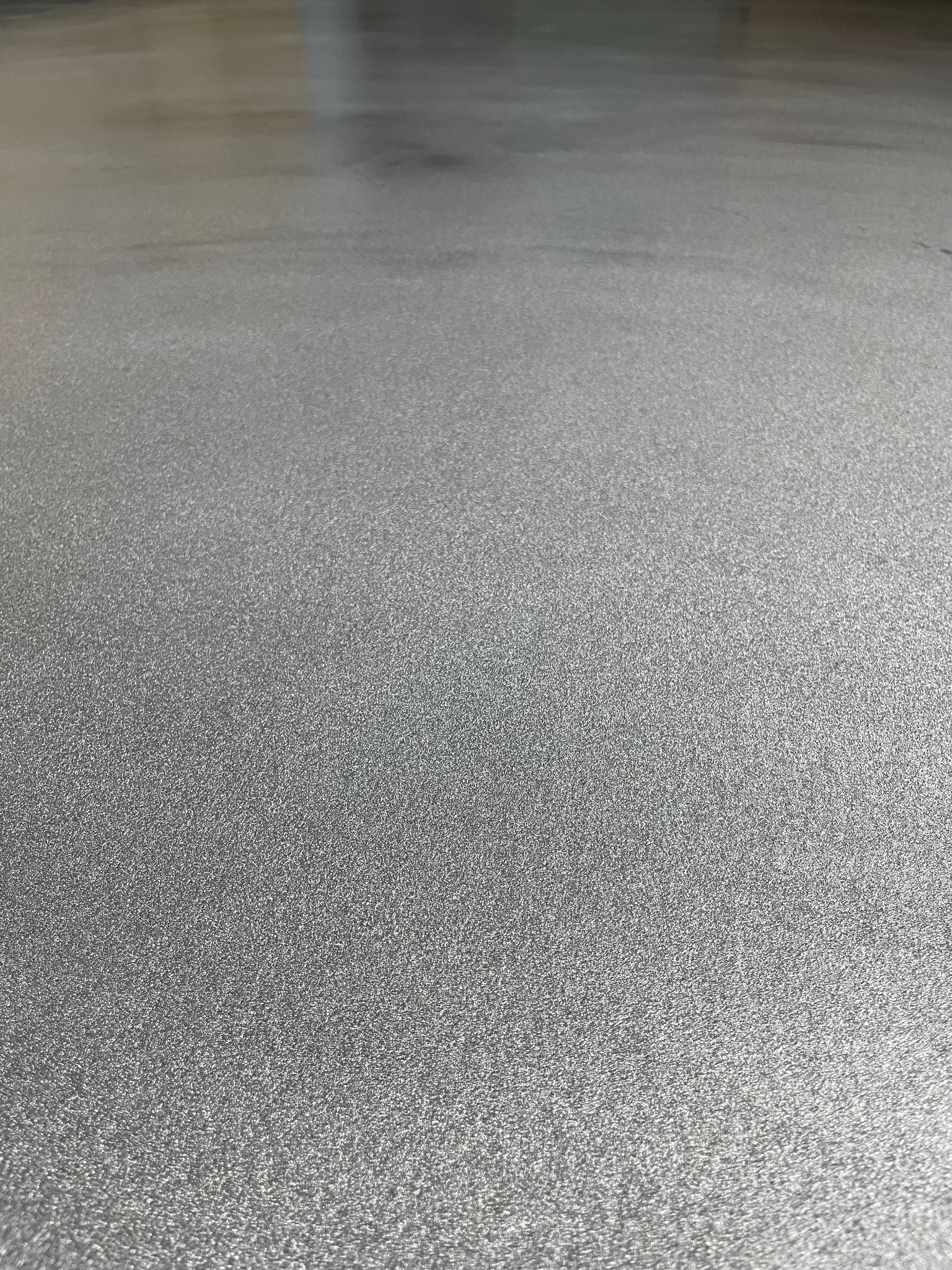 Jasnoszara, gładka posadzka z efektem delikatnego metalicznego połysku, widoczna z bliskiej perspektywy, oświetlona z góry.
