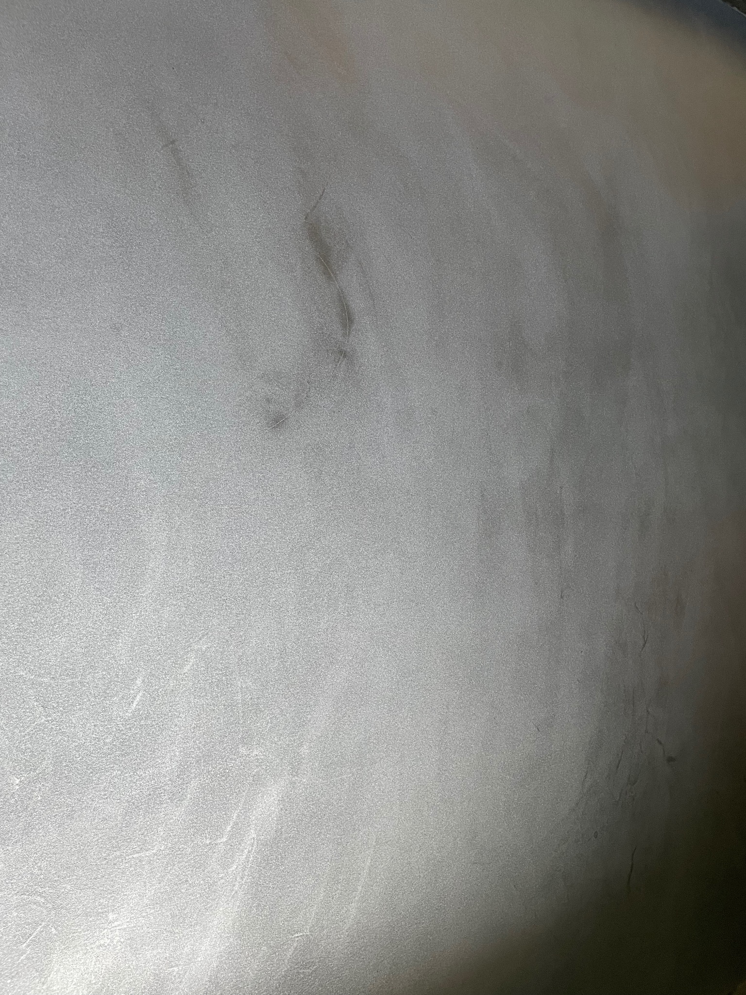 Szara, gładka powierzchnia z delikatną teksturą i ciemniejszymi smugami, przypominająca wykończenie podłogi lub ściany.