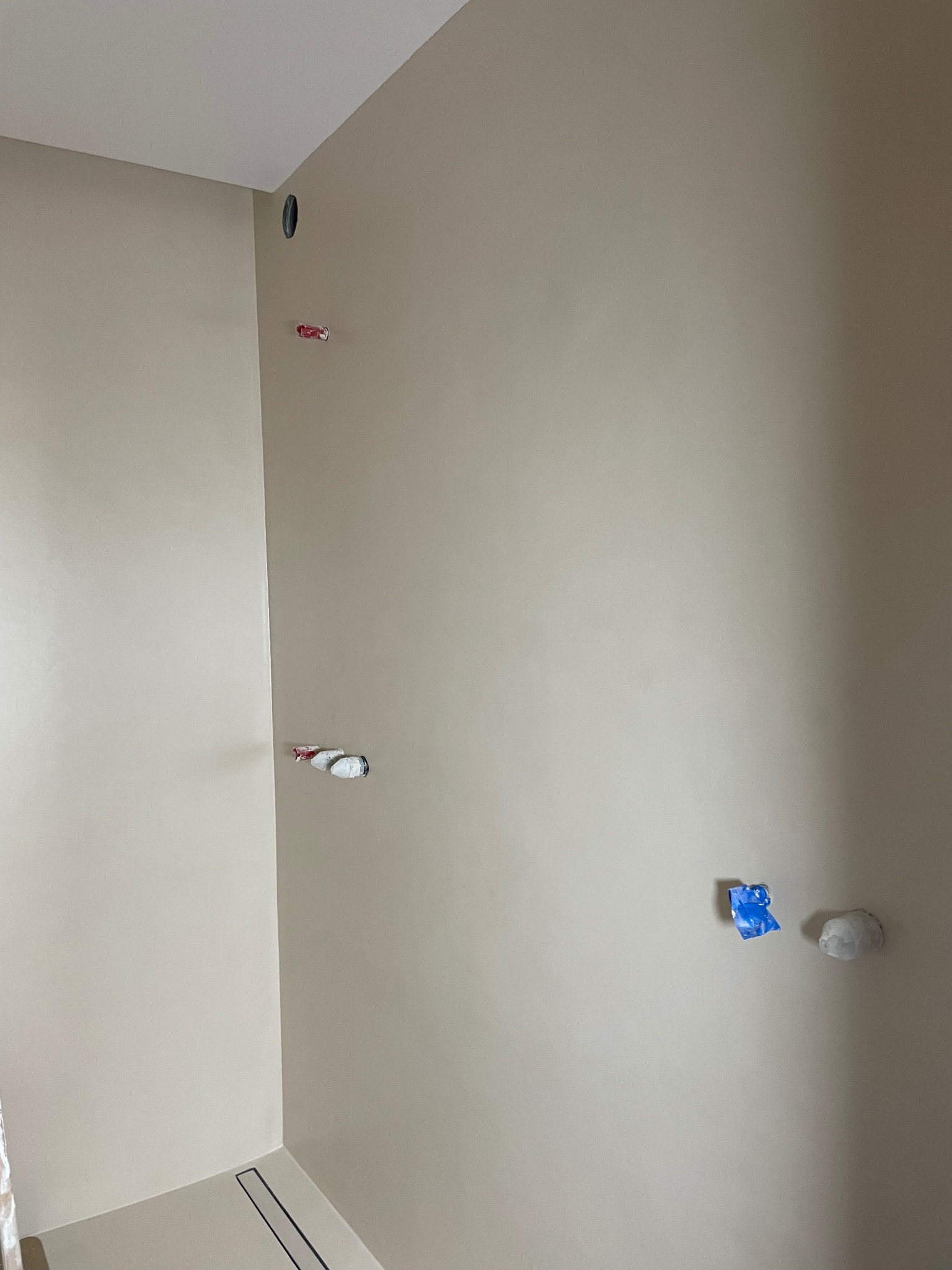 Beżowe ściany w nowym wnętrzu z widocznymi instalacjami wod-kan i elektrycznymi, przygotowane do wykończenia, z odpływem liniowym w podłodze.