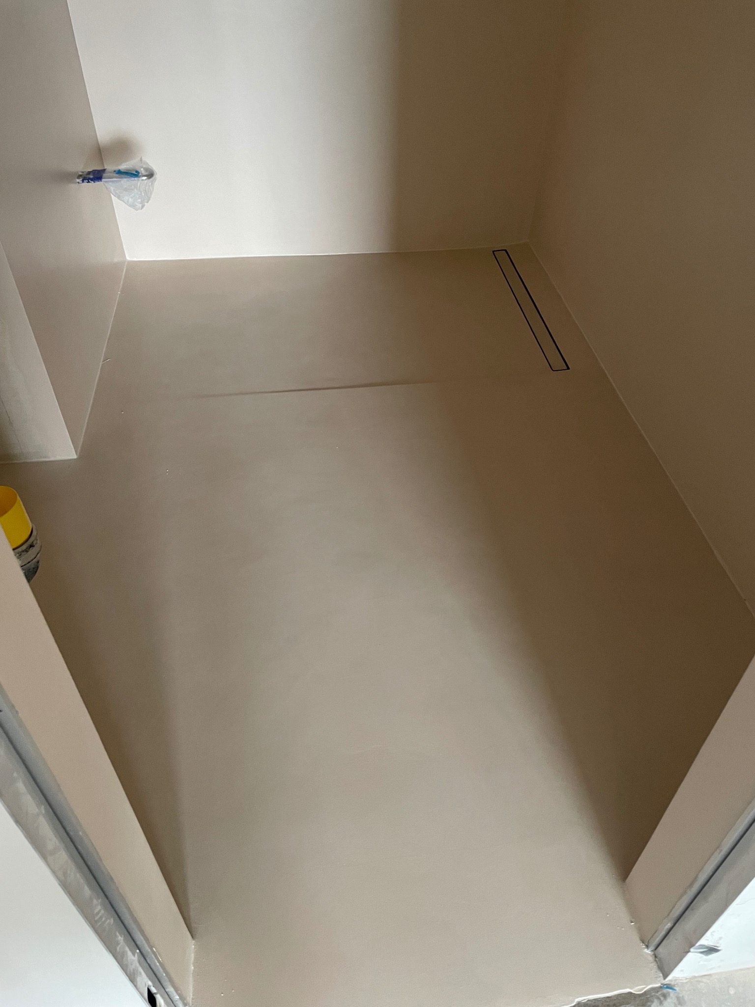 Jasna, beżowa powierzchnia z odpływem liniowym, świeżo po aplikacji. Widoczne detale wykończenia ścian i podłogi. W tle zakryta armatura.