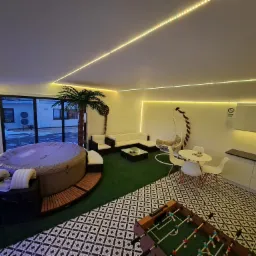 Nowoczesne wnętrze z jacuzzi, palmą, stołem do piłkarzyków i oświetleniem LED, tworzące relaksującą strefę rozrywki.