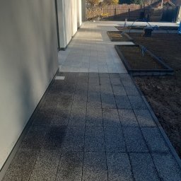 BrukPol - Ułożona dwukolorowa nawierzchnia z kostki brukowej przy nowoczesnym domu, z widocznymi rabatami kwiatowymi i elementami instalacji nawadniającej.