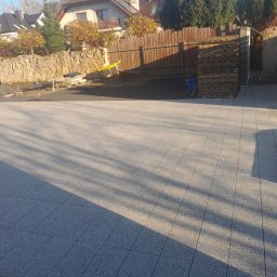 BrukPol - Ułożona jasnoszara nawierzchnia z kostki, widoczne palety, taczka i przygotowane podłoże pod dalsze prace, w tle ogrodzenie i dom.