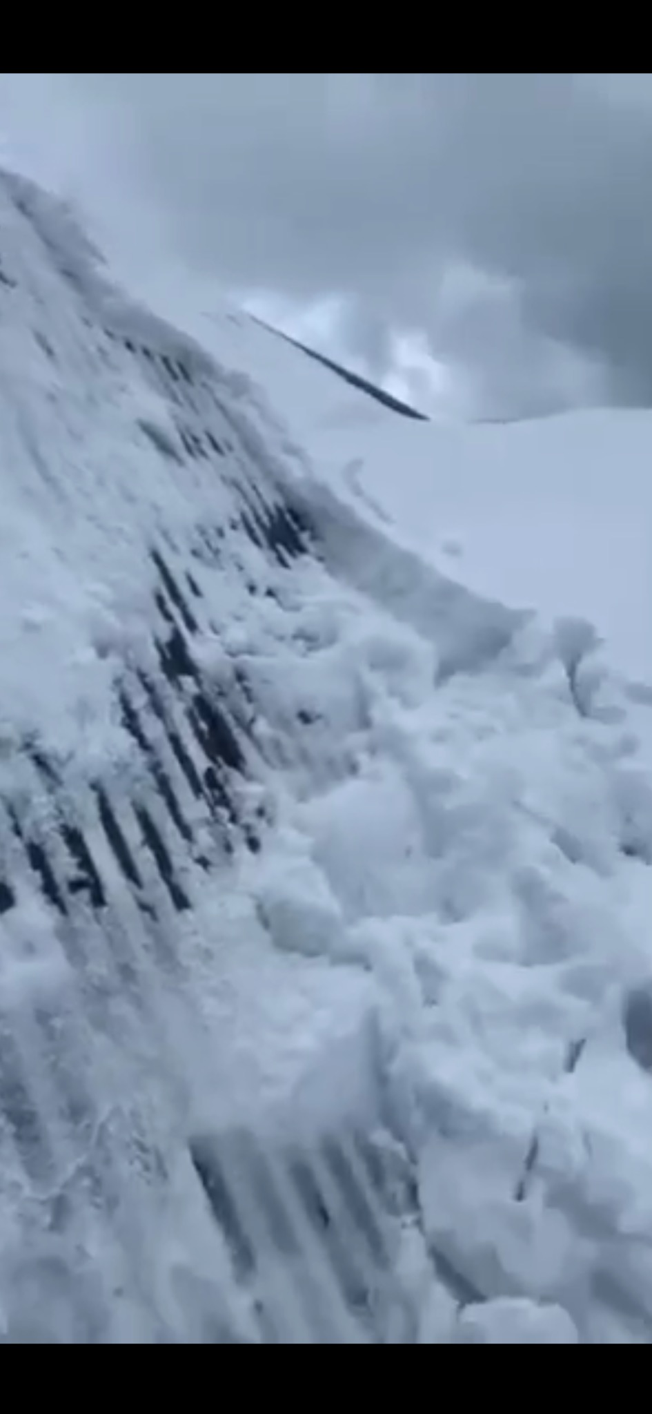 Śnieg zalega na dachu budynku z widocznymi fragmentami konstrukcji i śladami odśnieżania, pochmurne niebo w tle.