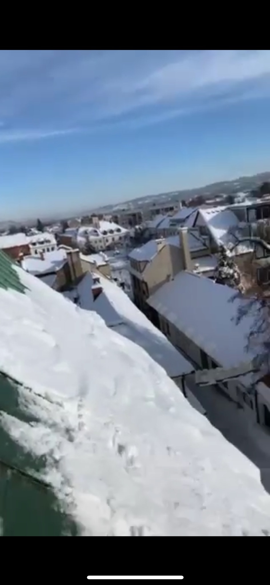 Śnieg zalegający na zielonym dachu budynku w miejskiej zabudowie, widok z góry, w tle błękitne niebo.