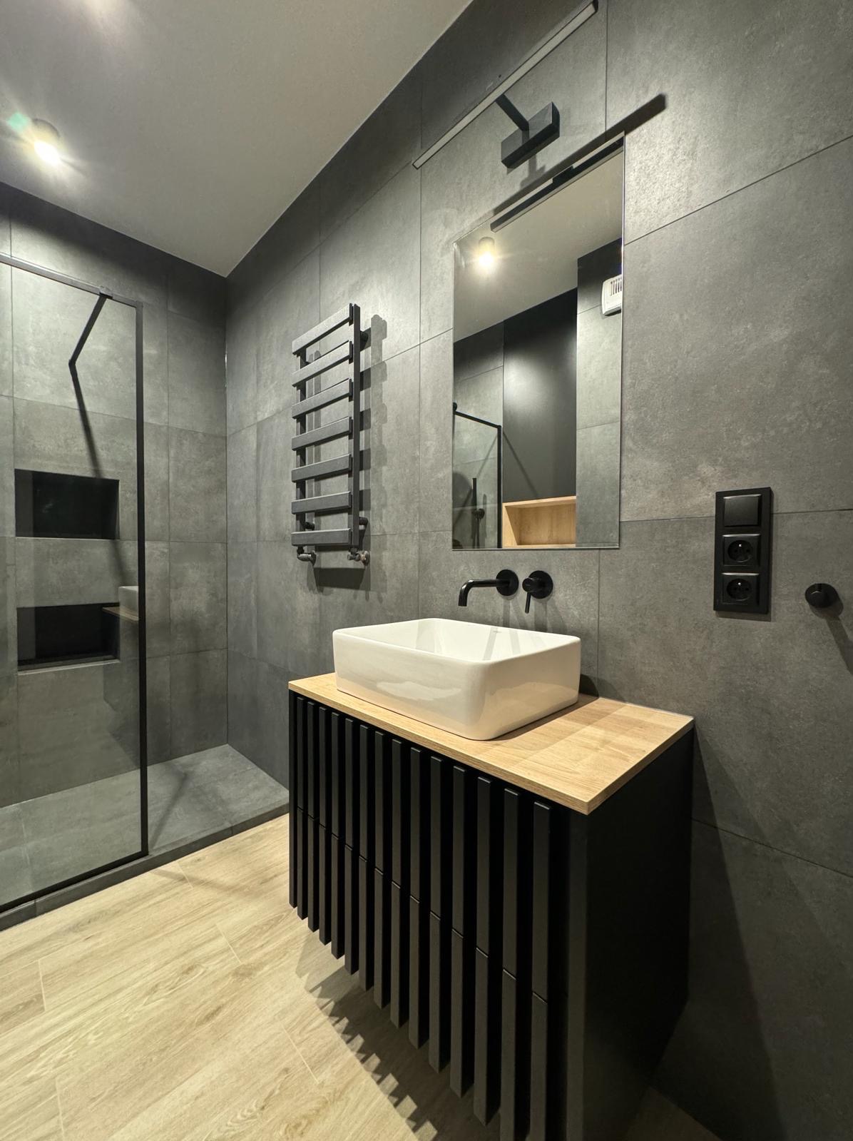 Nowoczesna łazienka w Poznaniu z szarymi płytkami, kabiną prysznicową typu walk-in, wiszącą szafką z umywalką nablatową i grzejnikiem drabinkowym.