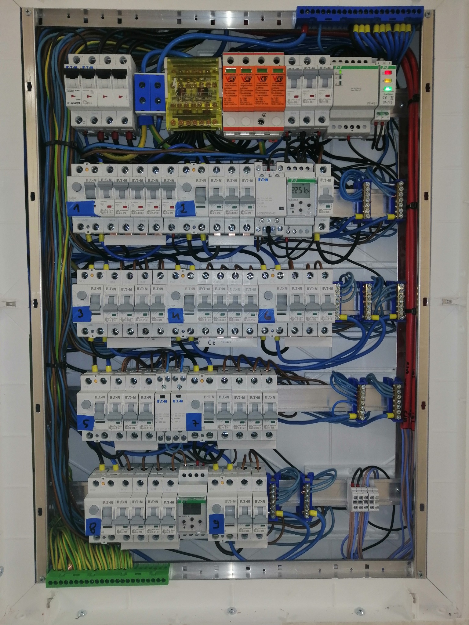 Rozdzielnica elektryczna z widocznymi zabezpieczeniami nadprądowymi, bezpiecznikami różnicowoprądowymi, przewodami w kolorach niebieskim, czarnym i zielono-żółtym, zabezpieczeniami...
