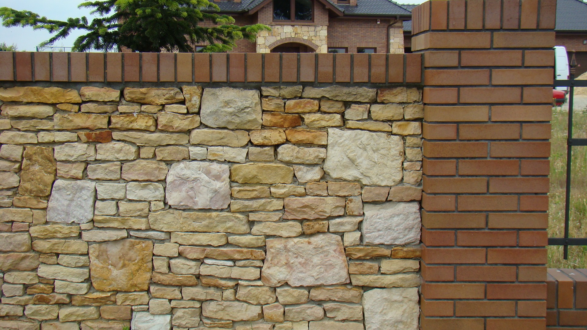 Kamienny mur z elementami ceglanymi w Oleśnicy, widok na fragment domu w tle.